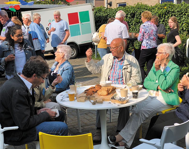 Bijeenkomst van Ressort Wonen met mensen aan een tafel met drankjes, cake en stroopwafels