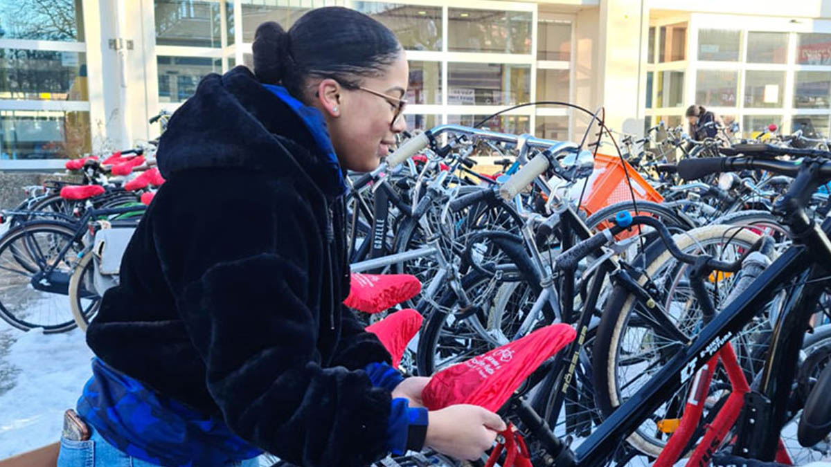 Vrouw die een rode zadelhoes om een fiets doet bij station Gouda